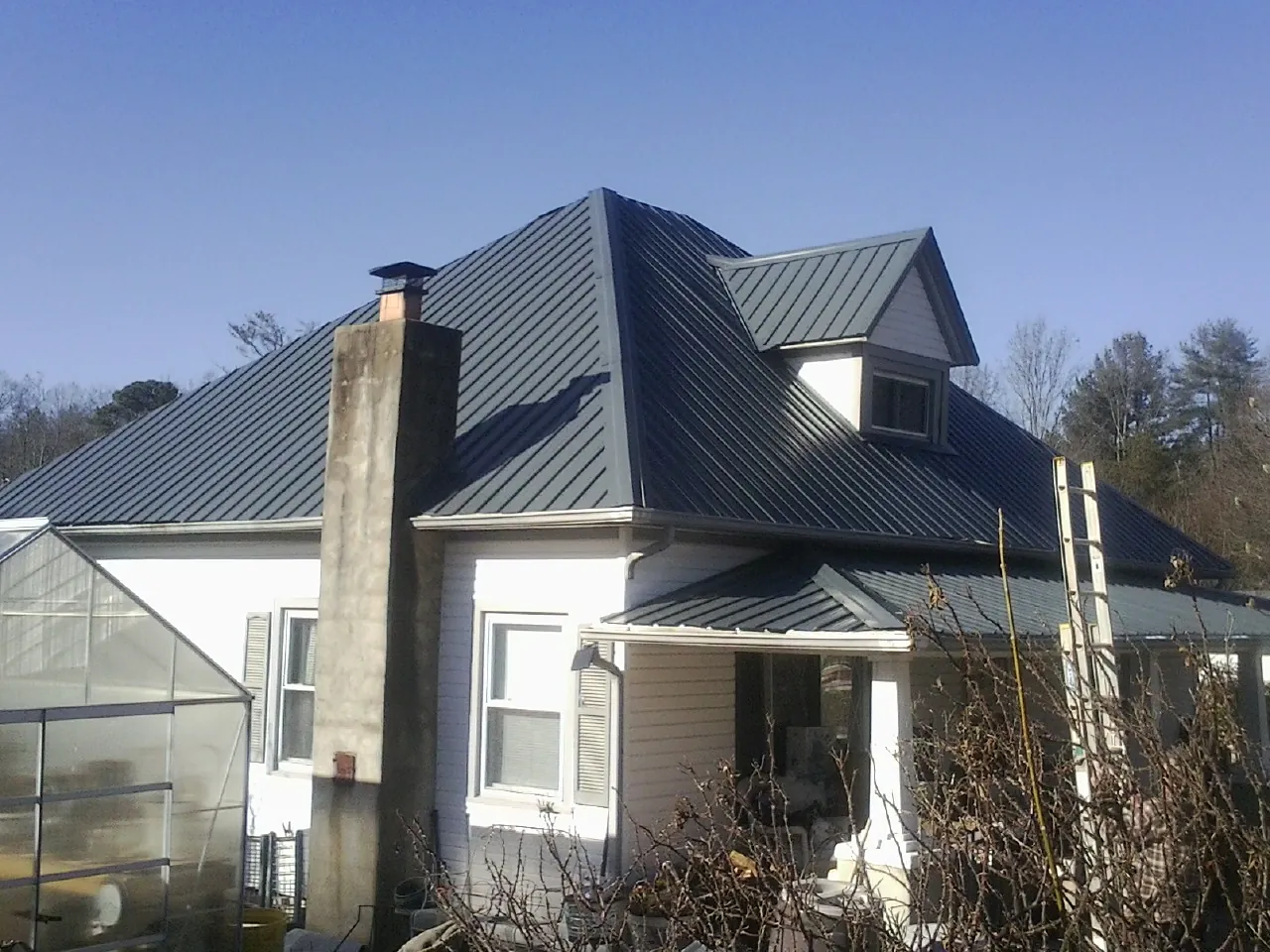 Dark blue standing seam metal roof on a white farmhouse with dormer — Slate & Tile Roof Repair by Roofing Brothers in Kingsland