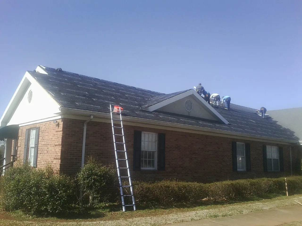 Crew tearing shingles off a brick ranch roof with a ladder set — Emergency Roof Repair work by our crew in Kingsland