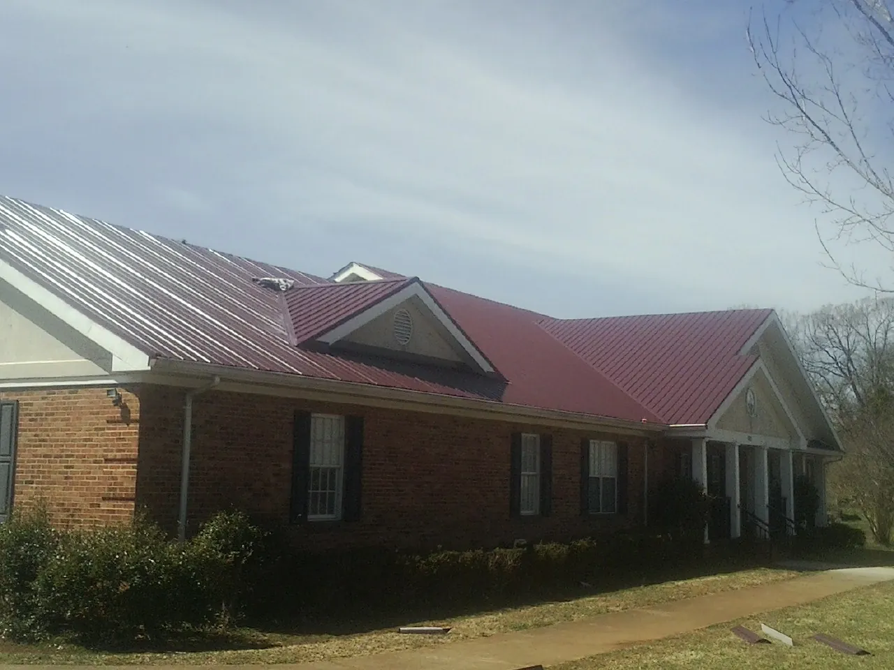 Red metal roof with gabled entries on a long brick building, from a Hail Damage Roof Repair job in Kingsland