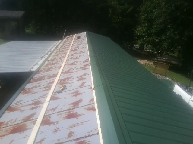 Old rusted panels beside newly installed green metal roofing — Wind Damage Roof Repair by Roofing Brothers in Kingsland