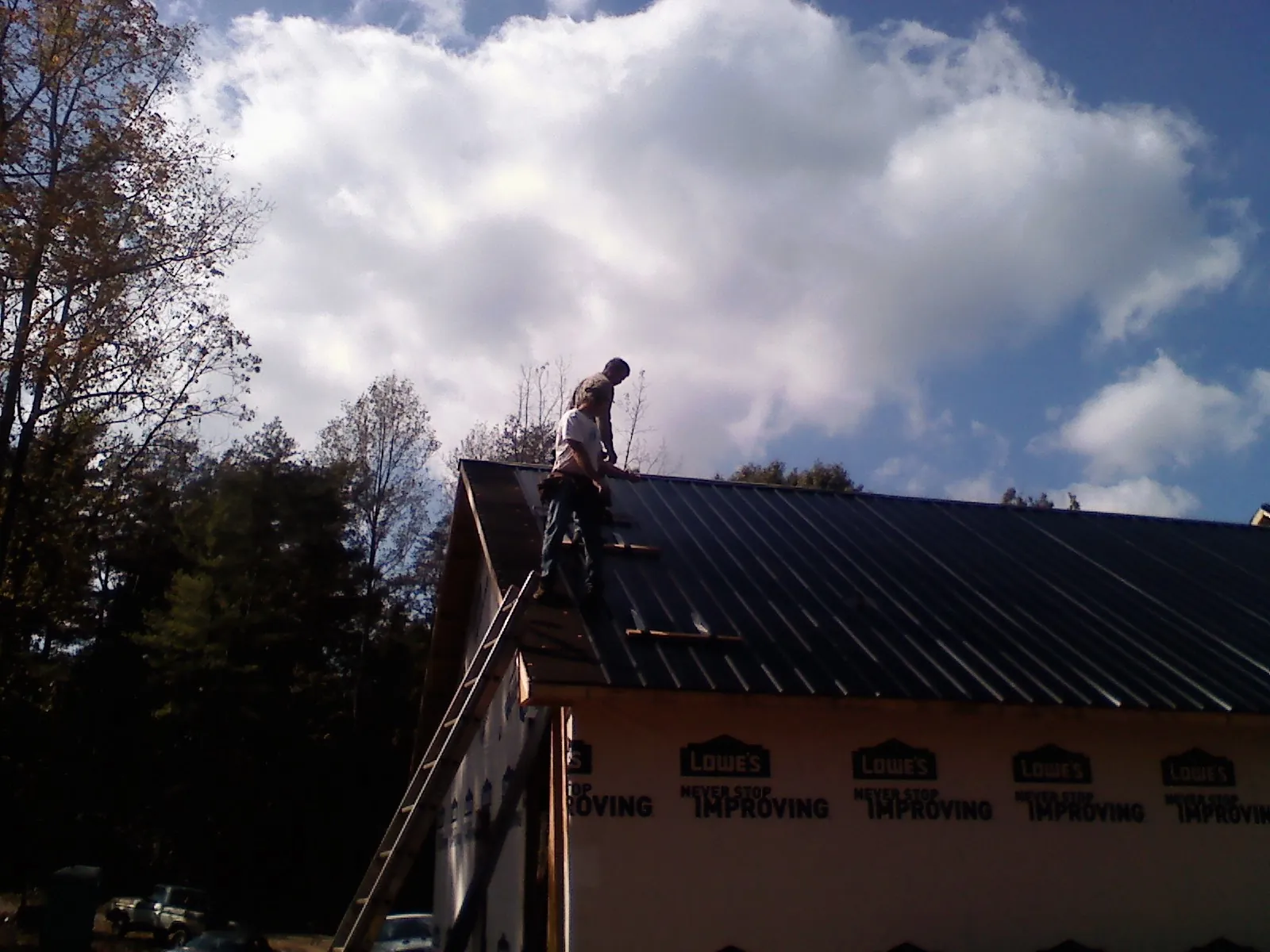 Roofer fastening dark metal panels high against a cloudy sky in Kingsland