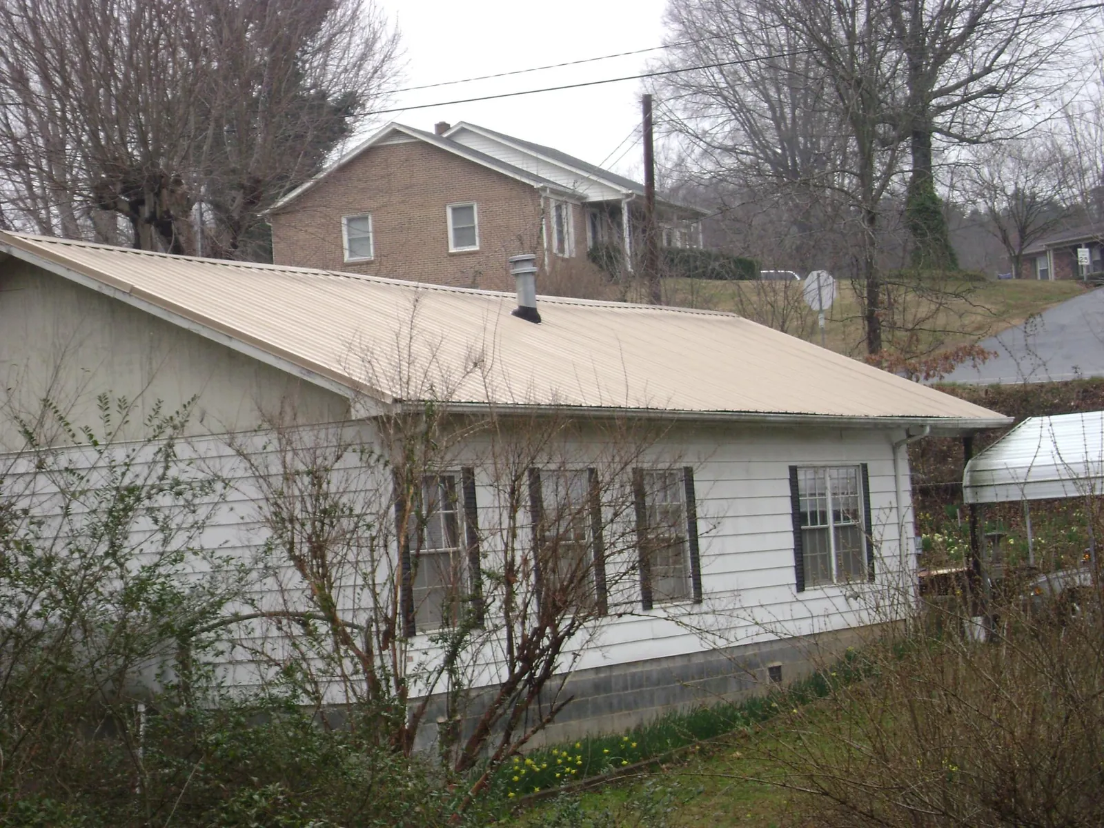 Tan metal roof on a white sided house set into a hillside — Commercial Roofing by Roofing Brothers in Kingsland